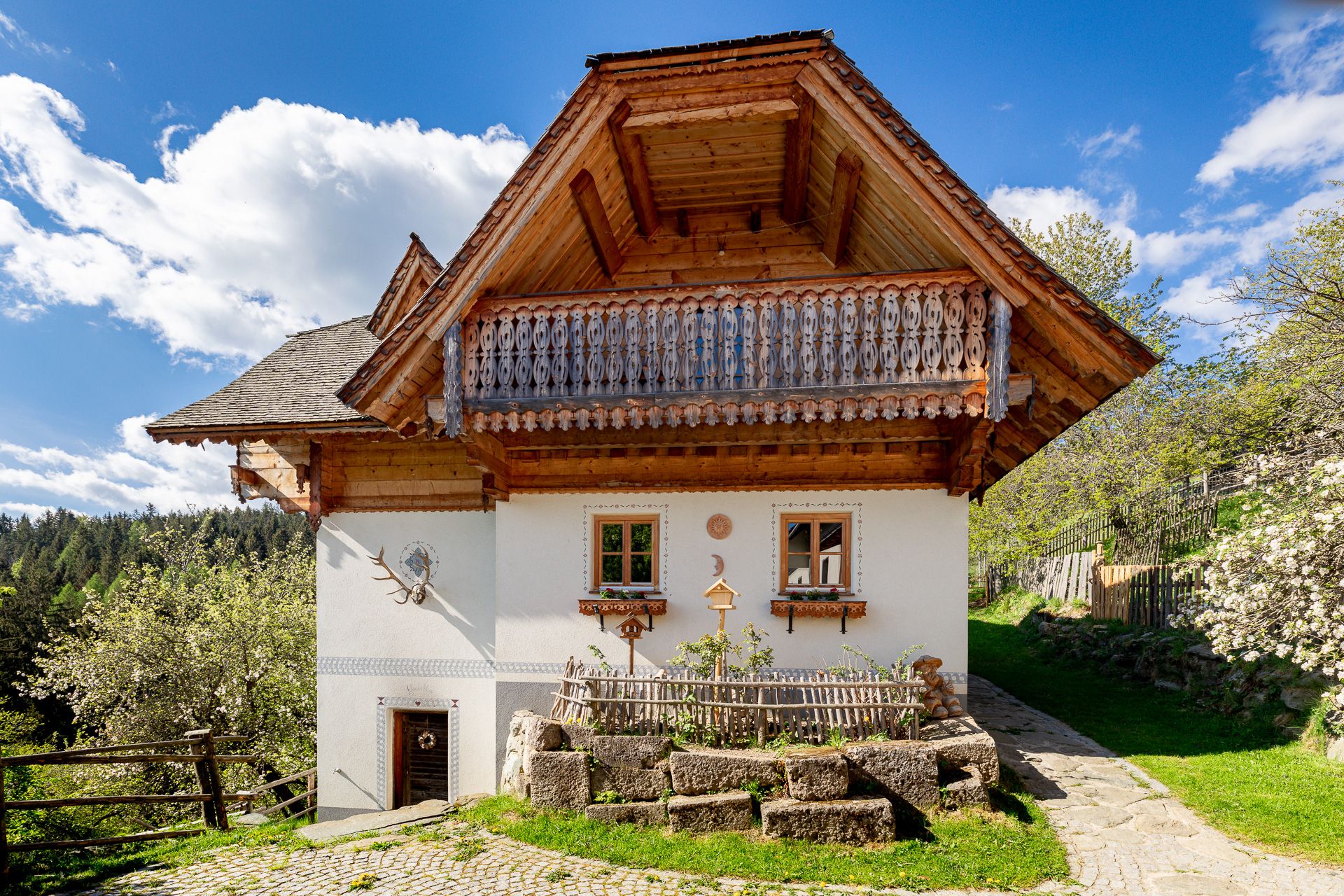 Traditional house with wooden balcony and white façade, surrounded by nature.