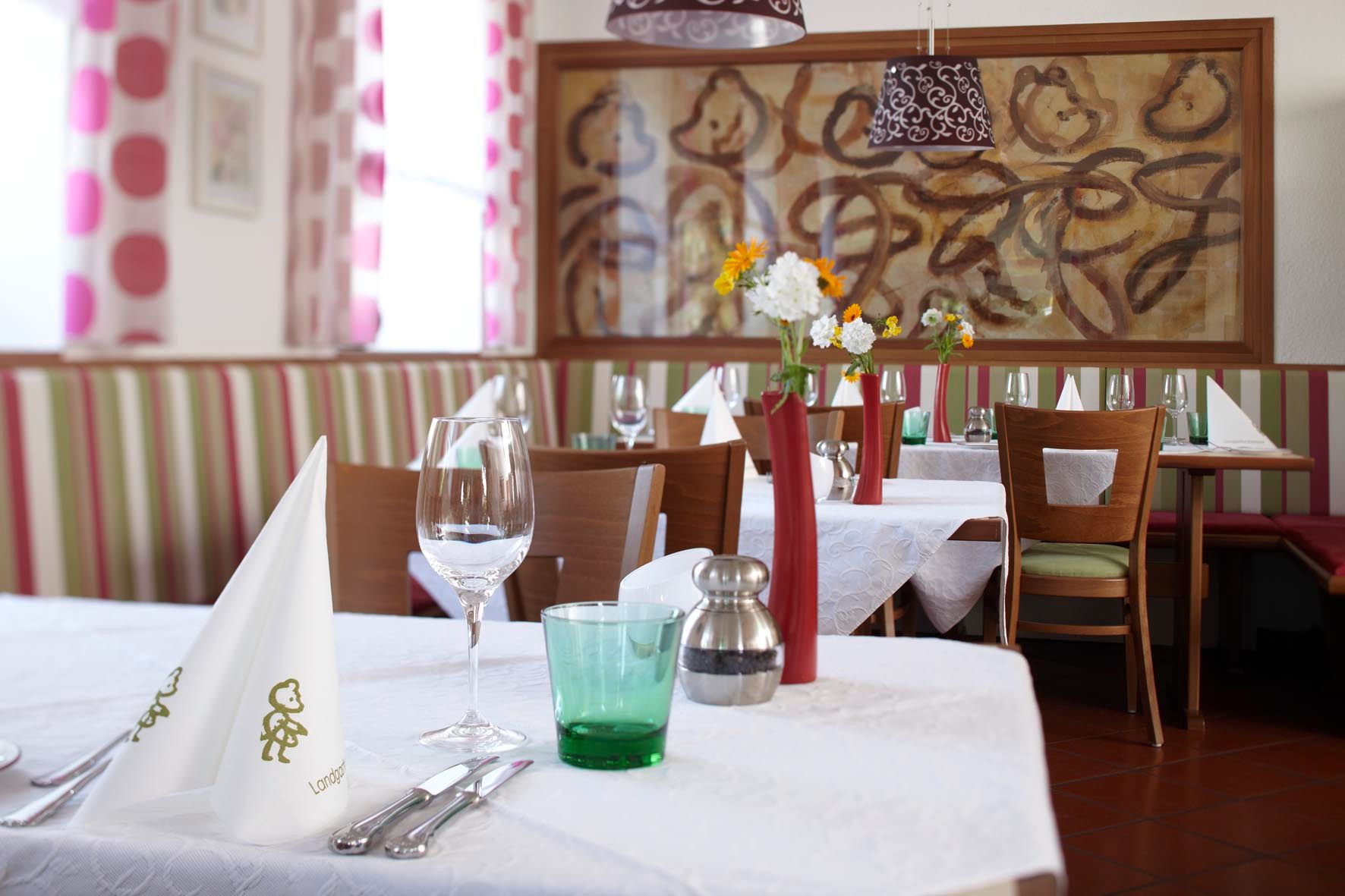 Interior view of a stylishly decorated restaurant with white tablecloths, flower vases and art on the wall.