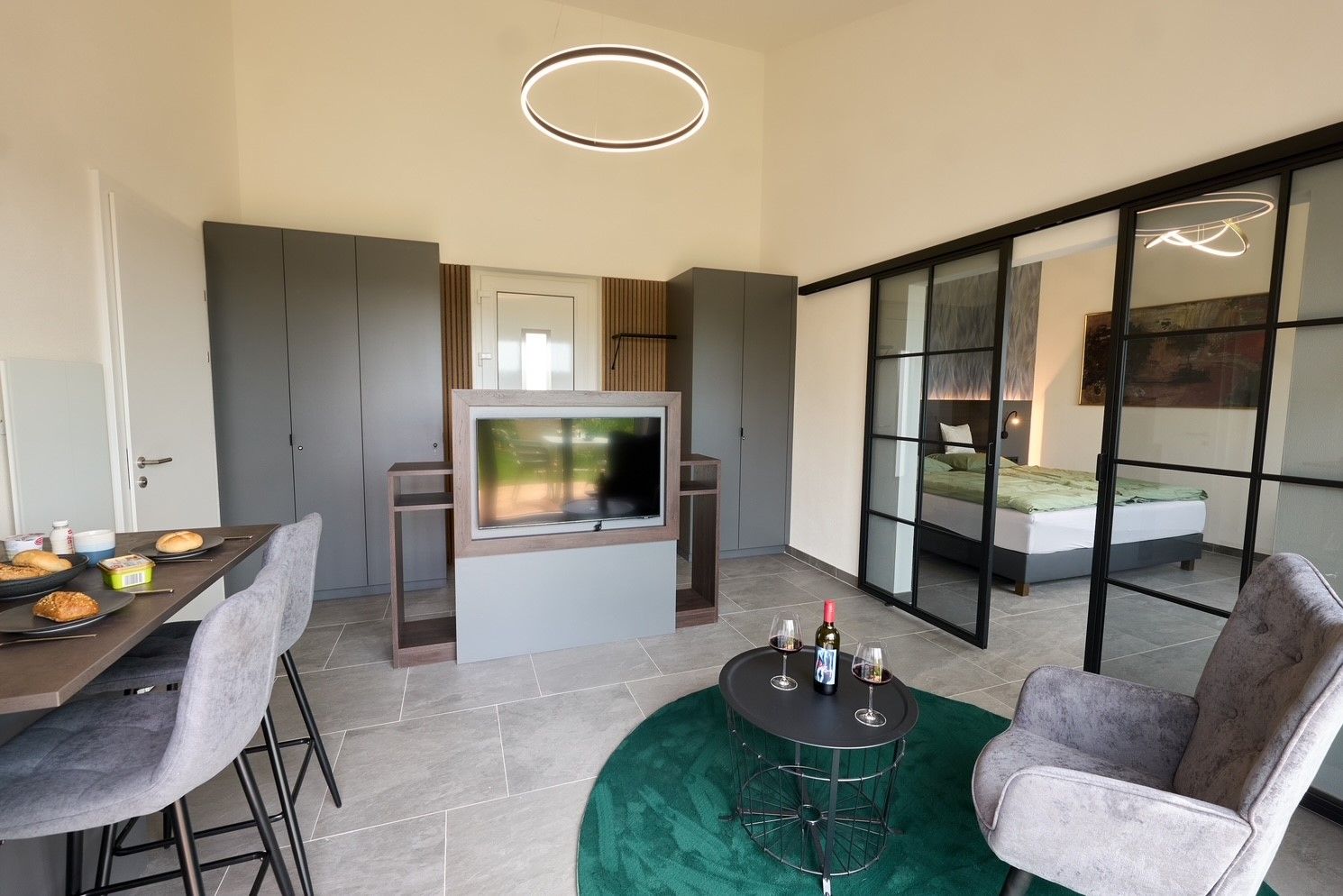 Modern apartment with dining table, TV, gray wardrobes and sliding glass doors to the bedroom.