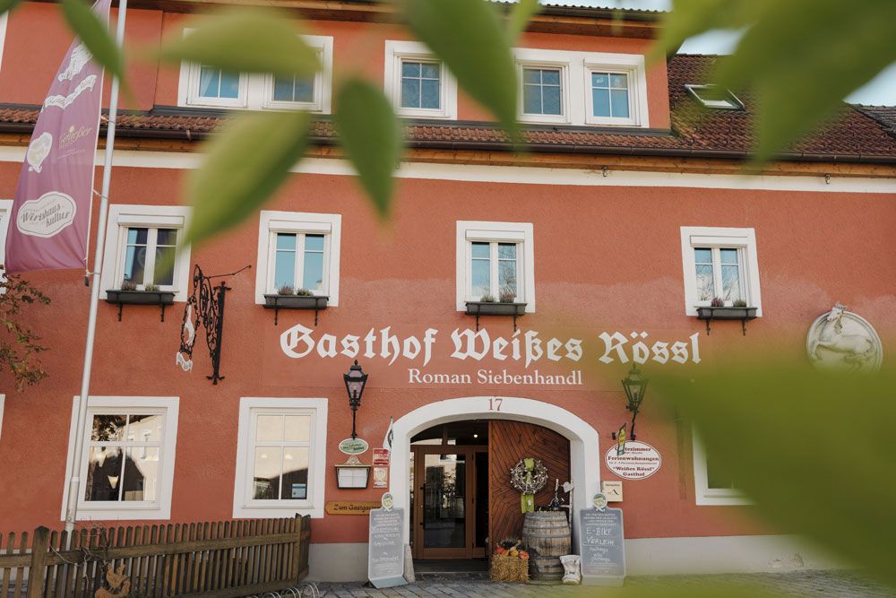 Facade of the Weißes Rössl inn in Mühldorf with red wall and white windows.