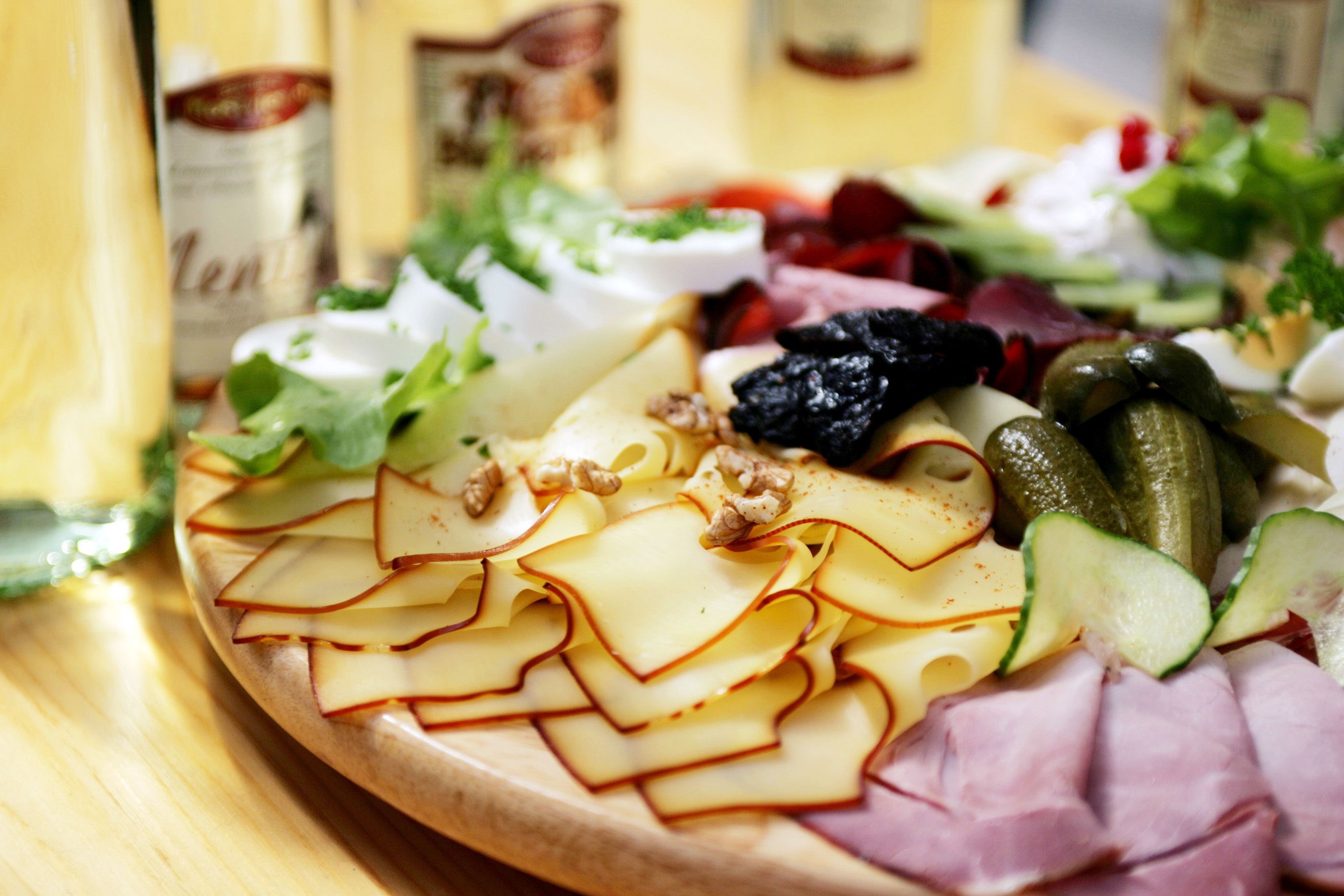 A snack board with cheese, ham, gherkins, nuts and salad on a wooden table.