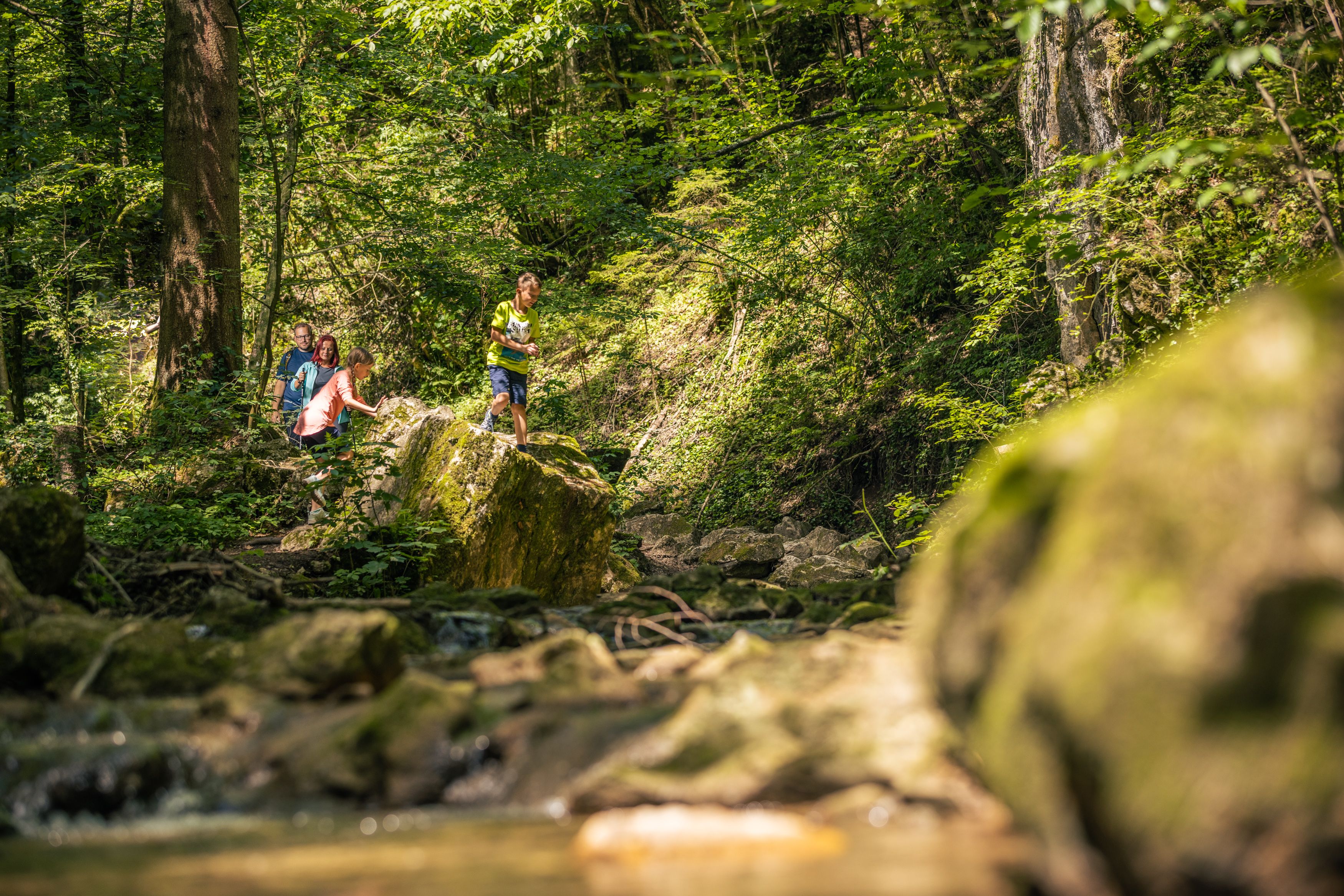Family hiking in the Johannesbachklamm gorge, surrounded by lush greenery and rocks.