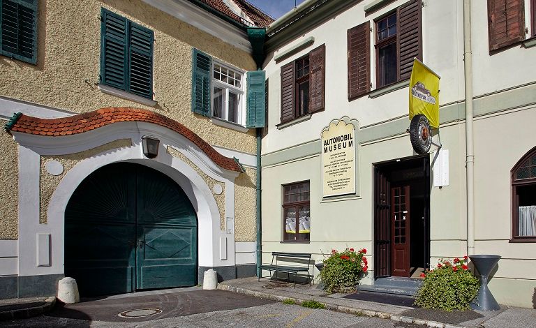 Entrance to an automobile museum with yellow flag and plants.