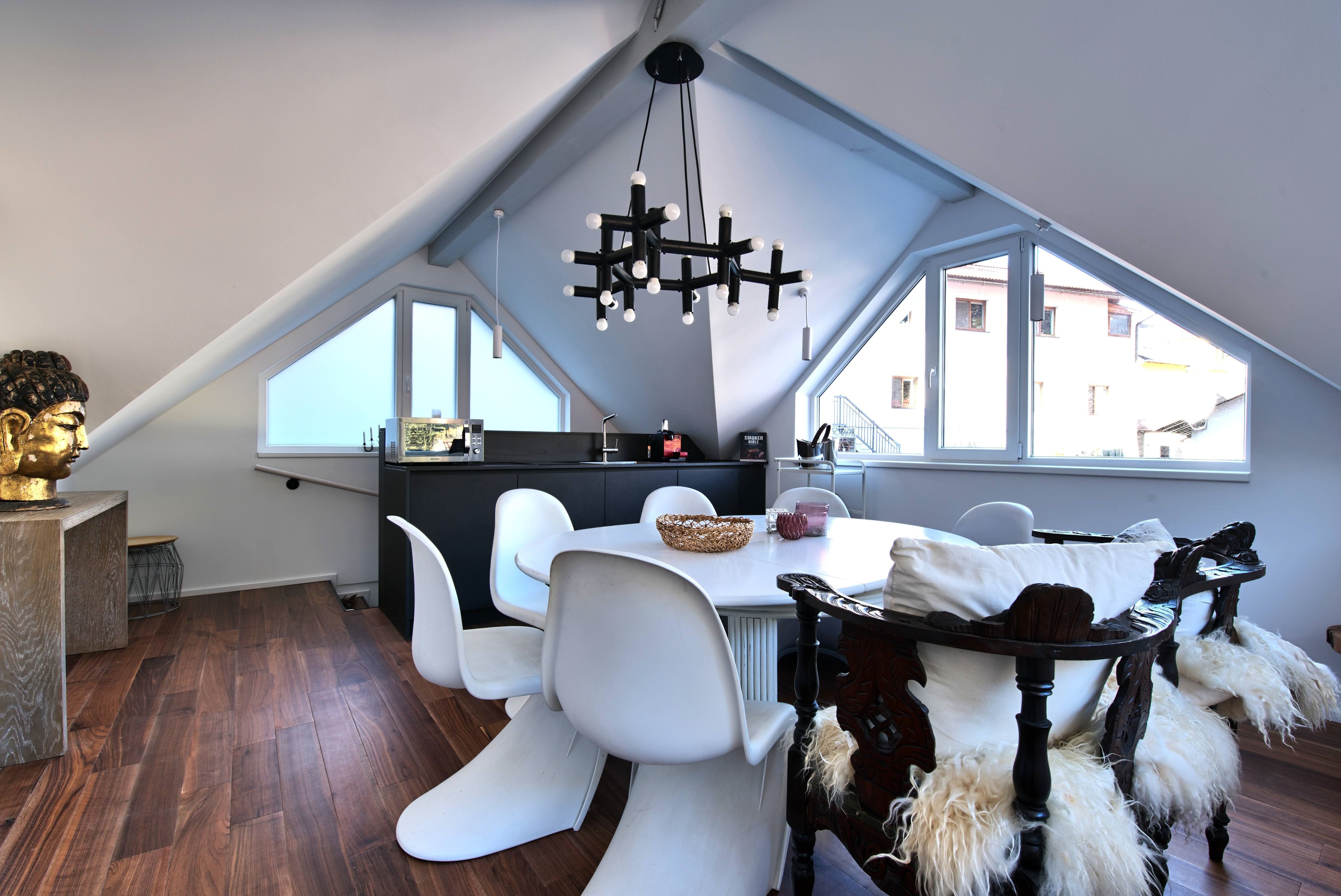 Modern dining area in a loft with white chairs, wooden floor and a large window.