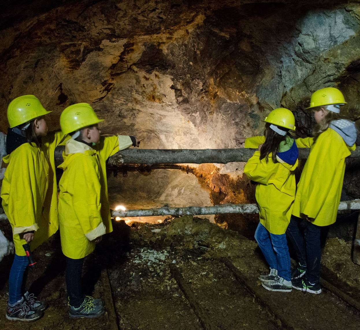 Children in yellow helmets and coats in a show mine.