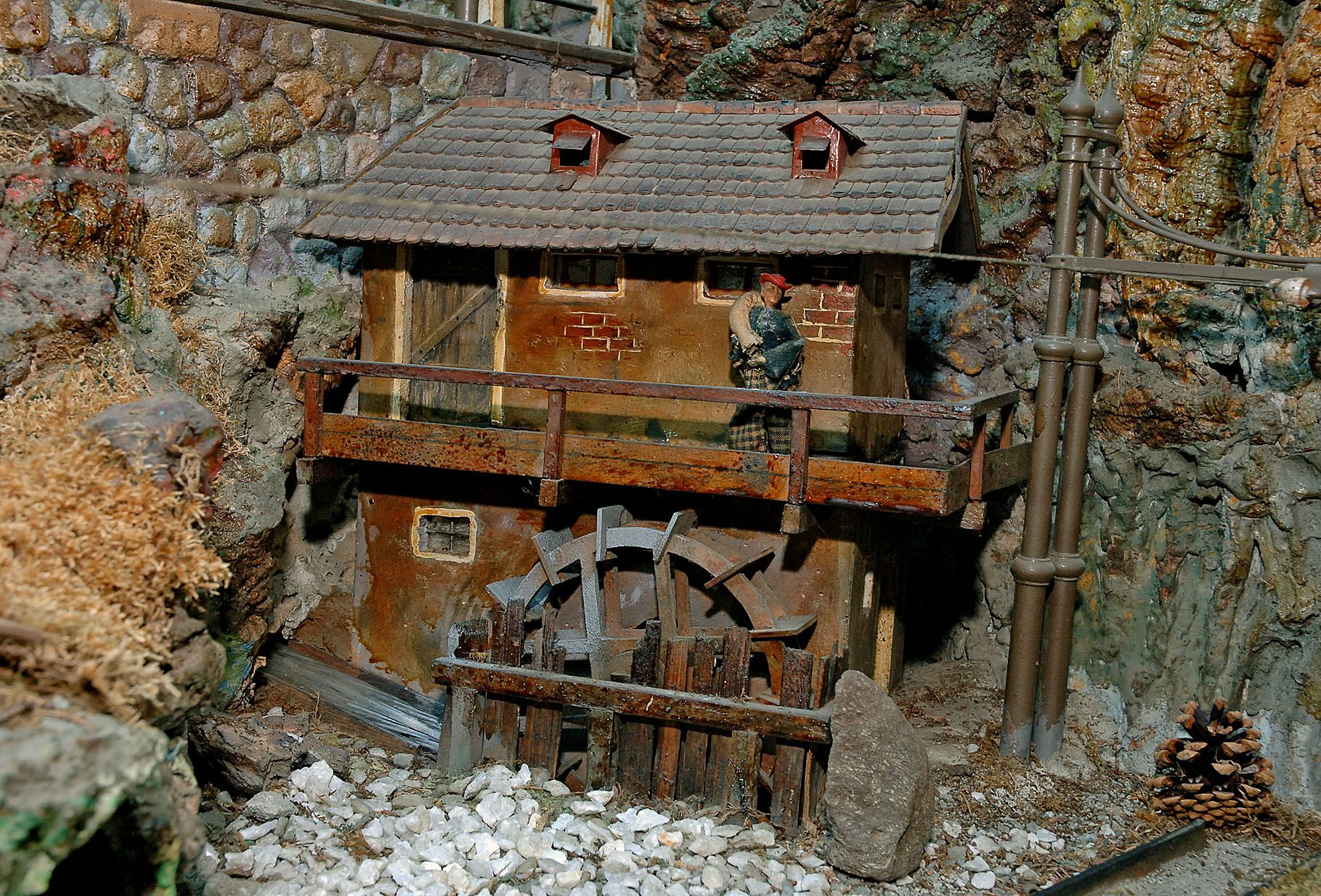 Miniature water mill with wooden wheel and small building in rocky surroundings.