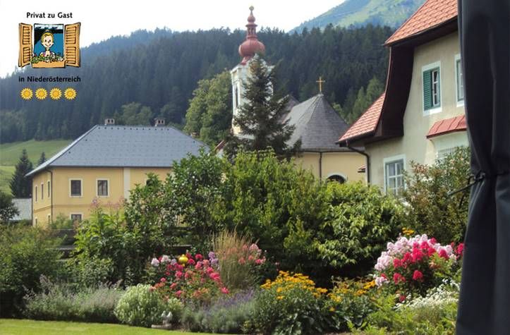 A picturesque garden with colorful flowers in front of traditional houses and a church in a mountainous landscape.