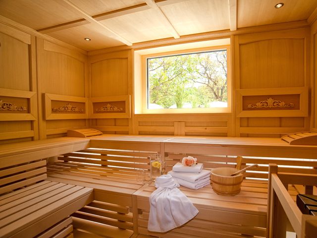 Interior view of a sauna with wooden benches, towels and a window with a view of the greenery.