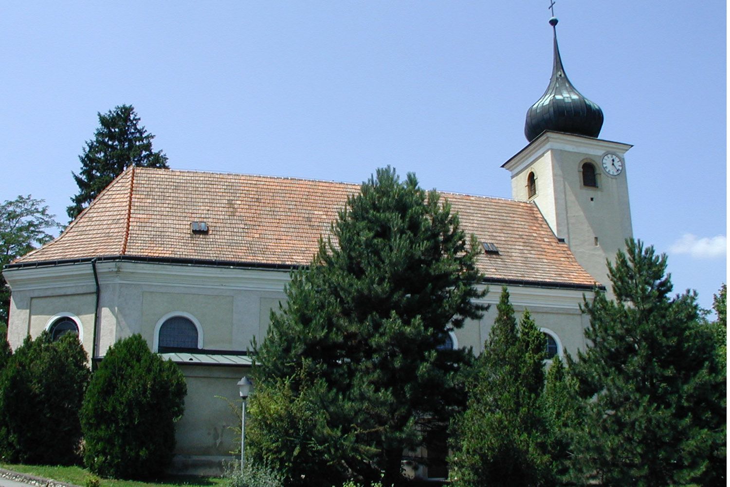 Church in Schleinbach with tower and clock, surrounded by trees.