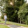 A woman walks barefoot on a green path in the spa gardens of Bad Schönau, surrounded by trees and sunlight.