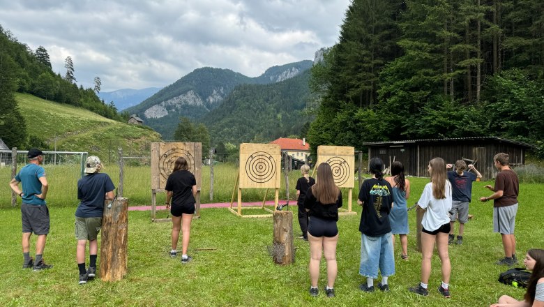 Group of people throwing axes outdoors in front of targets in a mountainous landscape.