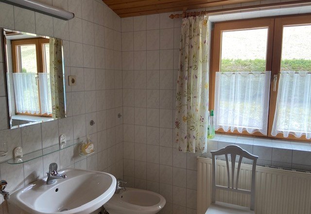 A bathroom with washbasin, bidet, mirror and window with curtains.