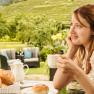 Woman enjoying coffee outdoors with a view of vineyards.