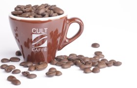 Brown cup with the inscription 'Cult Caffè', filled with coffee beans, on a white background.