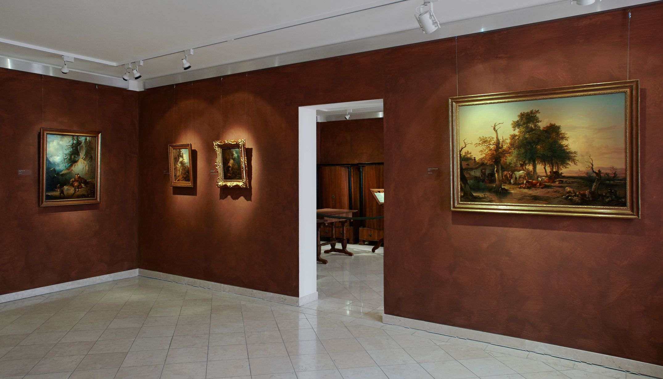 Interior view of a museum with paintings on brown walls.