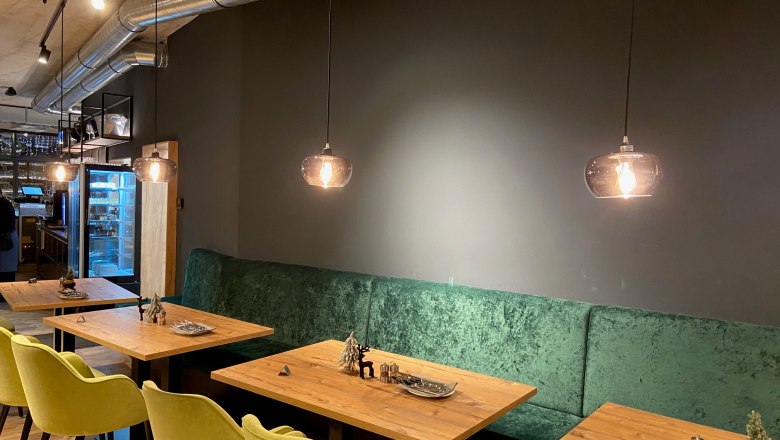 Interior view of a modern restaurant with wooden tables, green upholstered benches and hanging lamps.