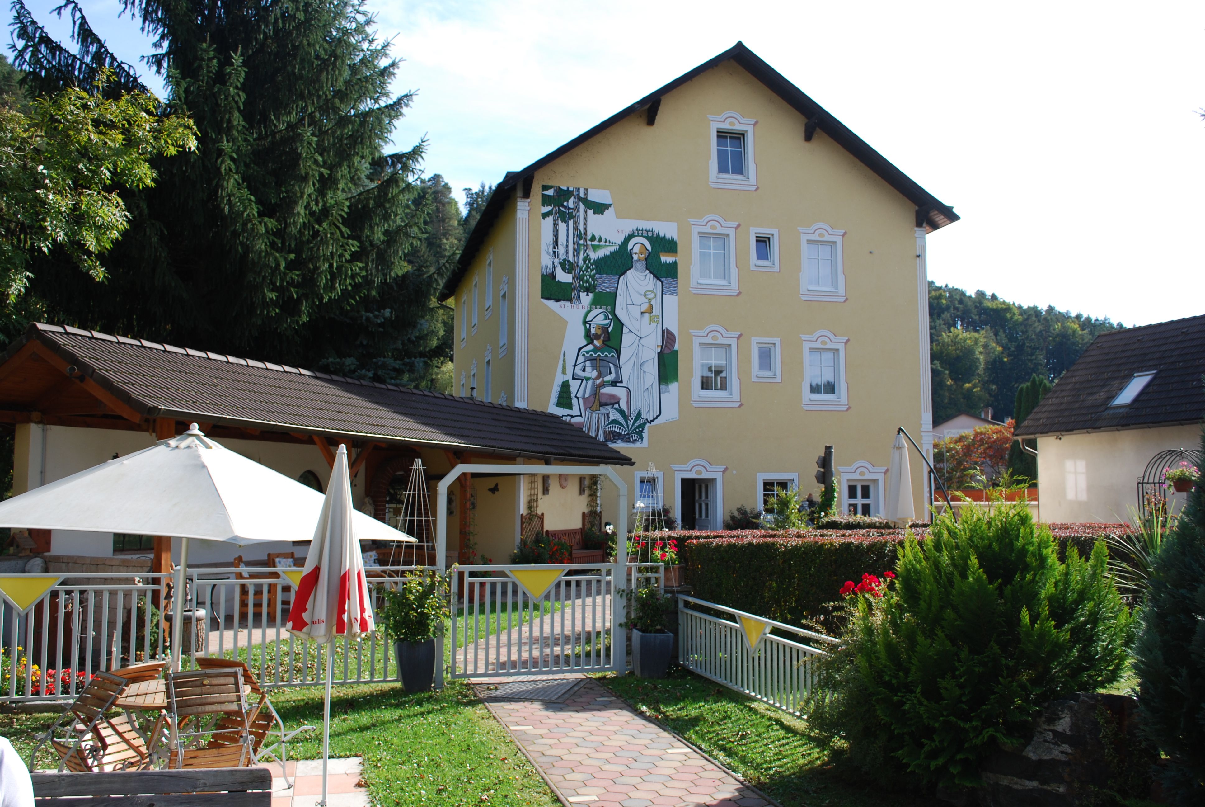 Yellow building with murals, garden with parasol and seating area.