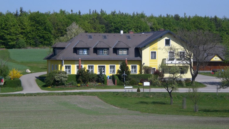 A yellow inn in a rural setting with trees and meadows.