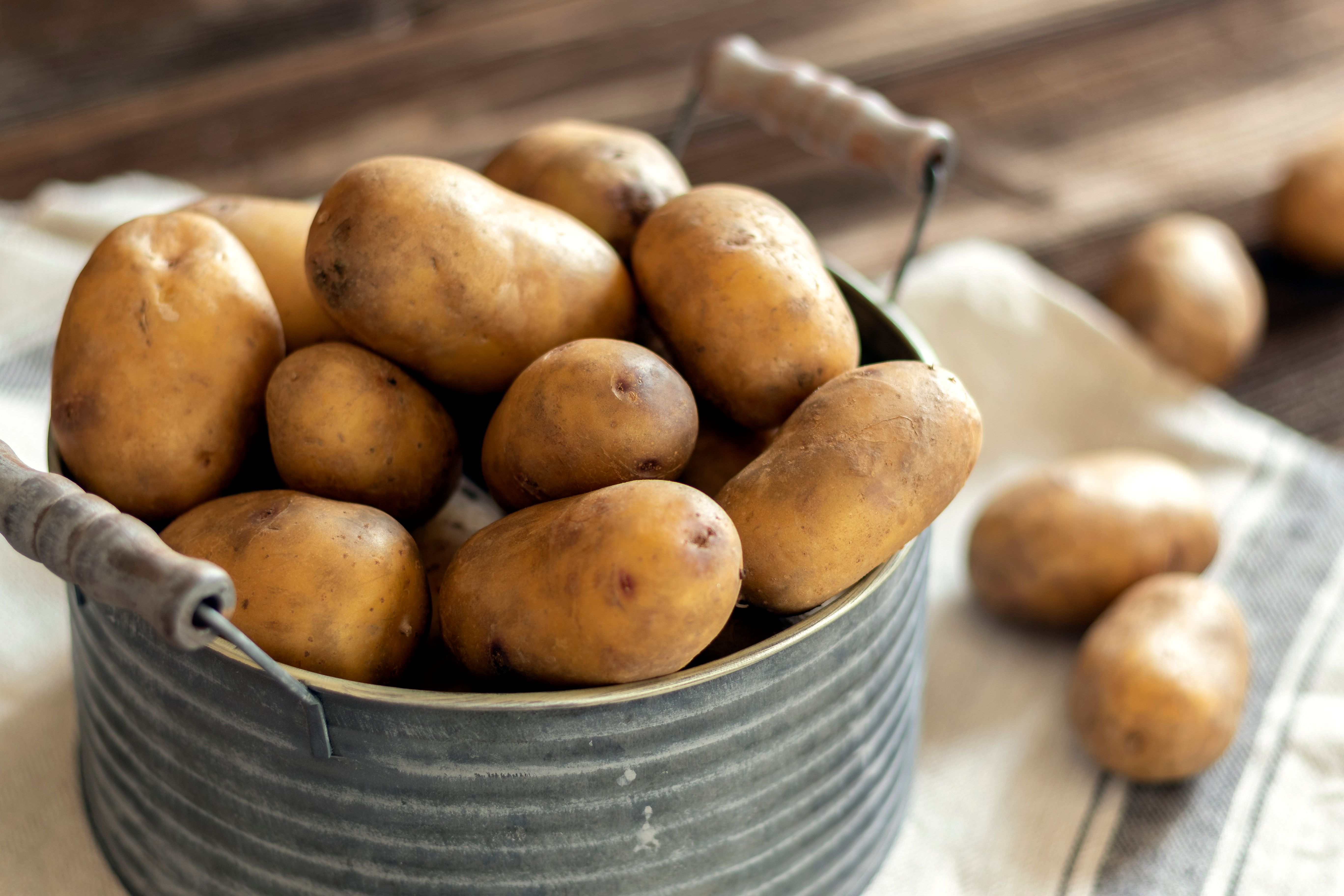 A pot filled with potatoes on a cloth, in the background even more potatoes.
