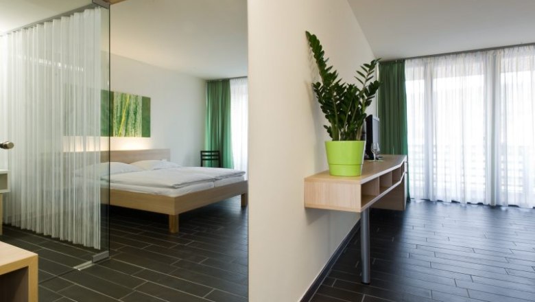 Modern hotel room with double bed, green curtain and houseplant.