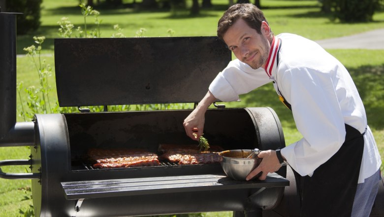 A cook grills meat on a large outdoor grill.