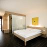 Modern hotel room with double bed, wooden furniture and glass wall.