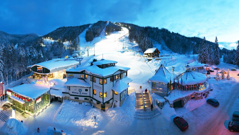 Winter ski station at dusk with illuminated buildings and slopes.
