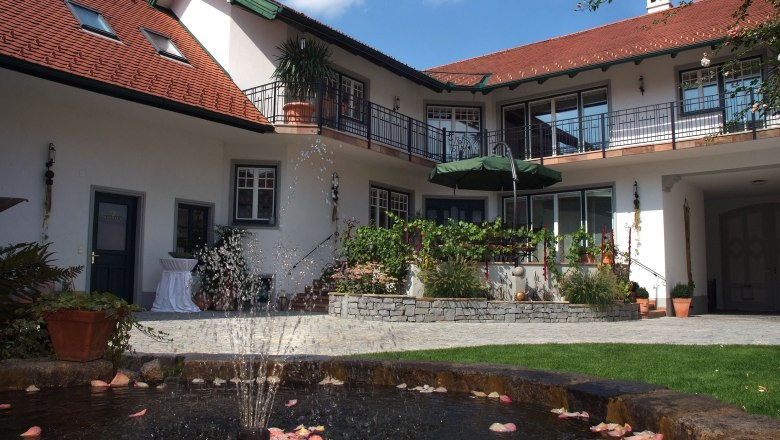 An inner courtyard with a fountain, surrounded by a two-storey building with red roofs and balconies.