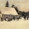 Historical postcard of a ski resort with people on skis in front of a hut in the snow.