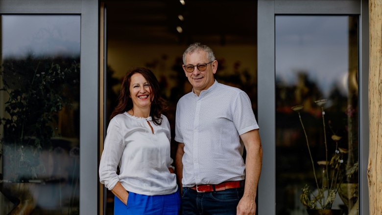 A man and a woman stand smiling in front of a glass door.