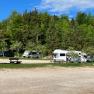 Motorhomes on a pitch in the countryside with trees and benches.