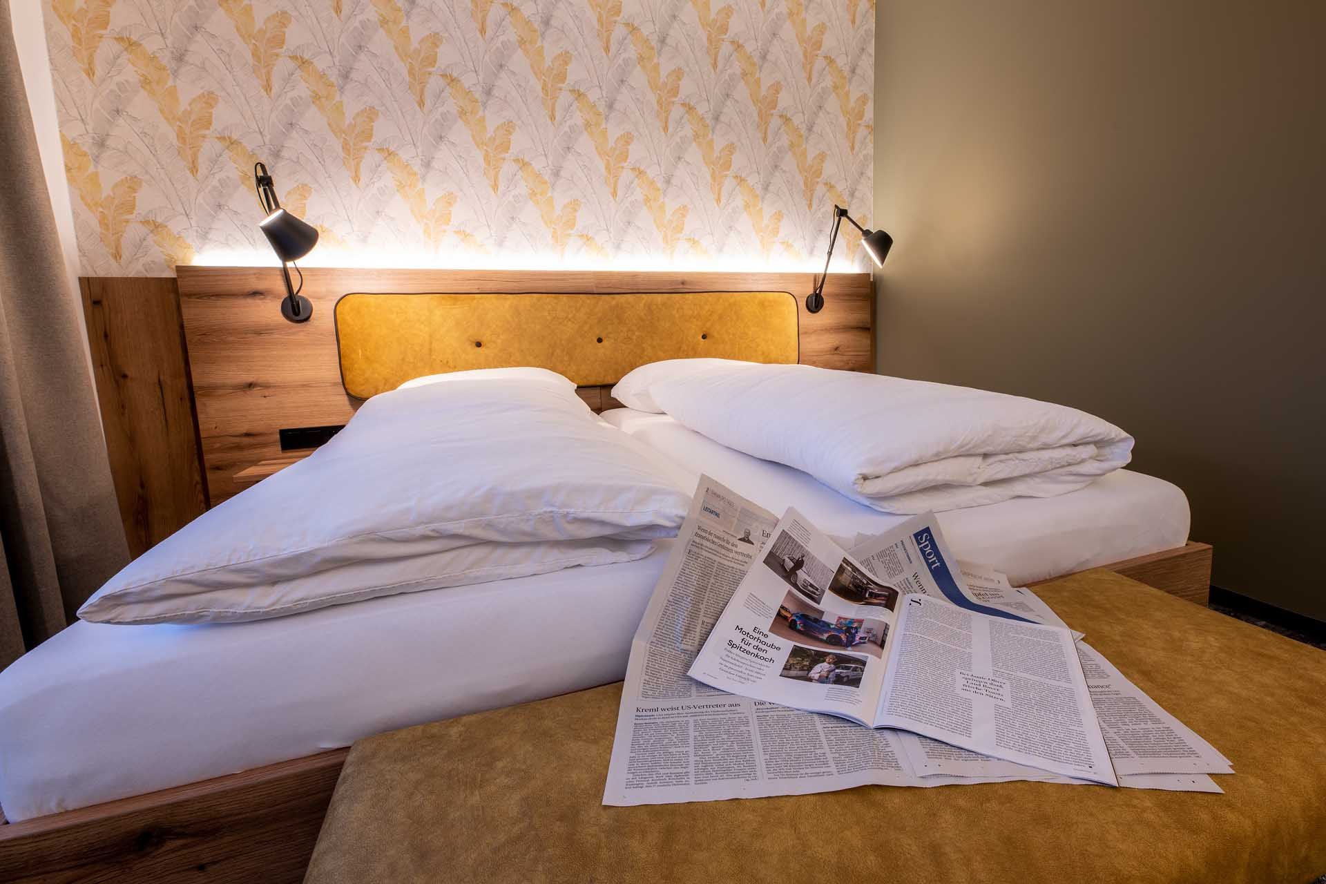 Cozy guest room with double bed, newspapers on the bedspread and stylish wallpaper in the background.