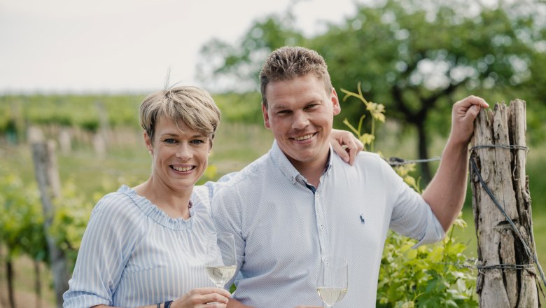 Two people in a vineyard with wine glasses.