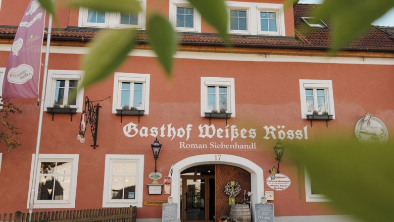 Facade of the Wei&szlig;es R&ouml;ssl inn in M&uuml;hldorf with red wall and white windows.