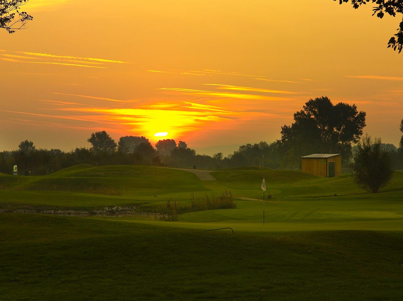 Sunset over a golf course with flag and small building.