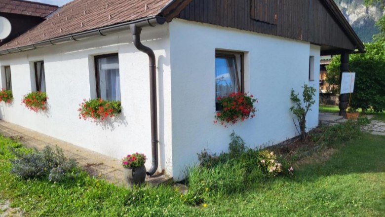 White house with red flowers in flower boxes in front of the windows, green meadow in the foreground.