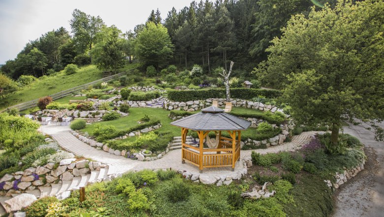 A wooden pavilion in a well-tended garden with green trees and stone paths.