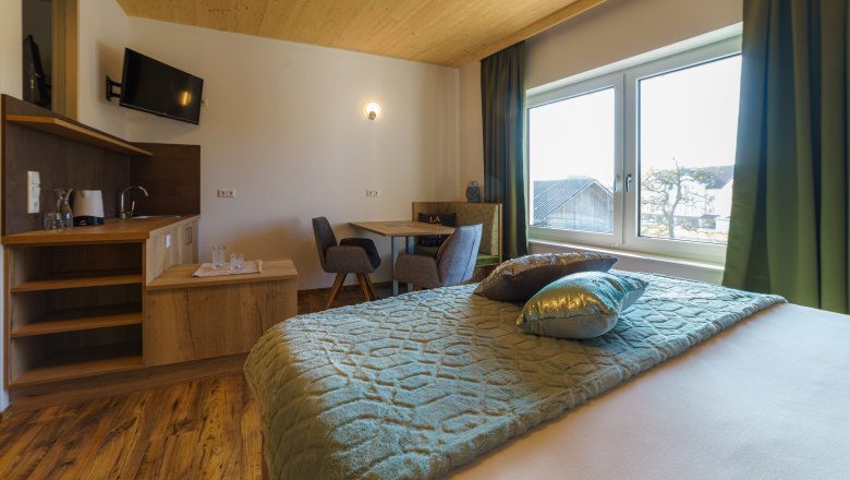 Comfortable hotel room with wooden floor, double bed, small table and chairs, TV and large window with a view.