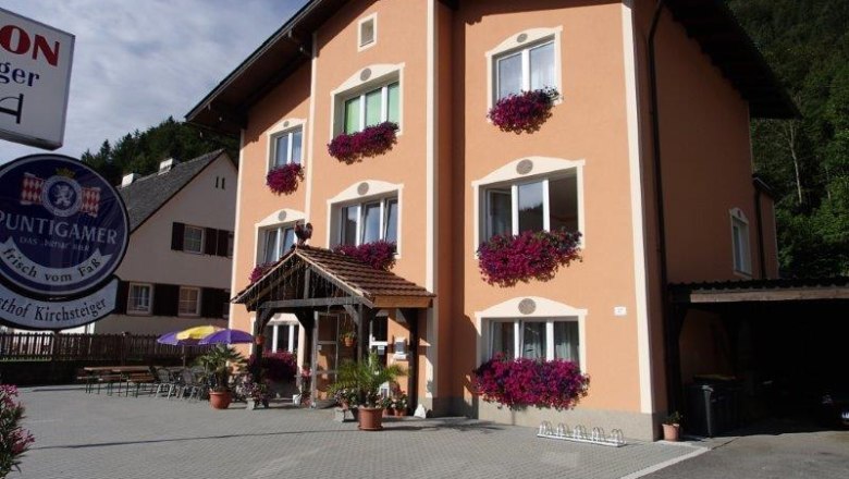 A three-storey building with an orange fa&ccedil;ade and flower boxes in front of the windows. A sign with the inscription 'Puntigamer' is visible.