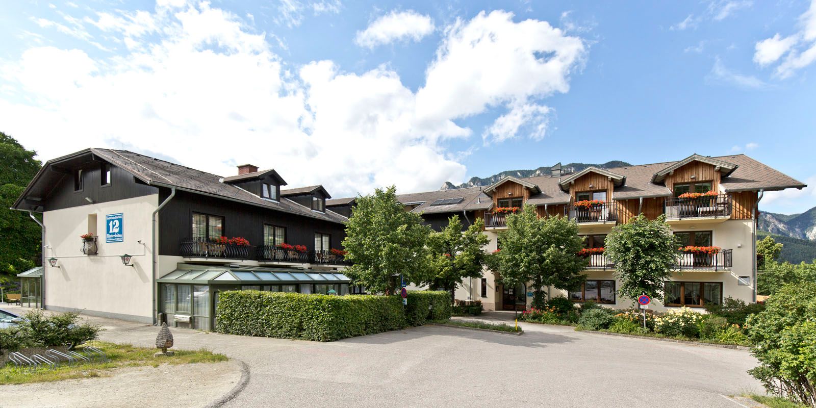 A traditional inn with wooden balconies and flower boxes, surrounded by trees and mountains in the background.