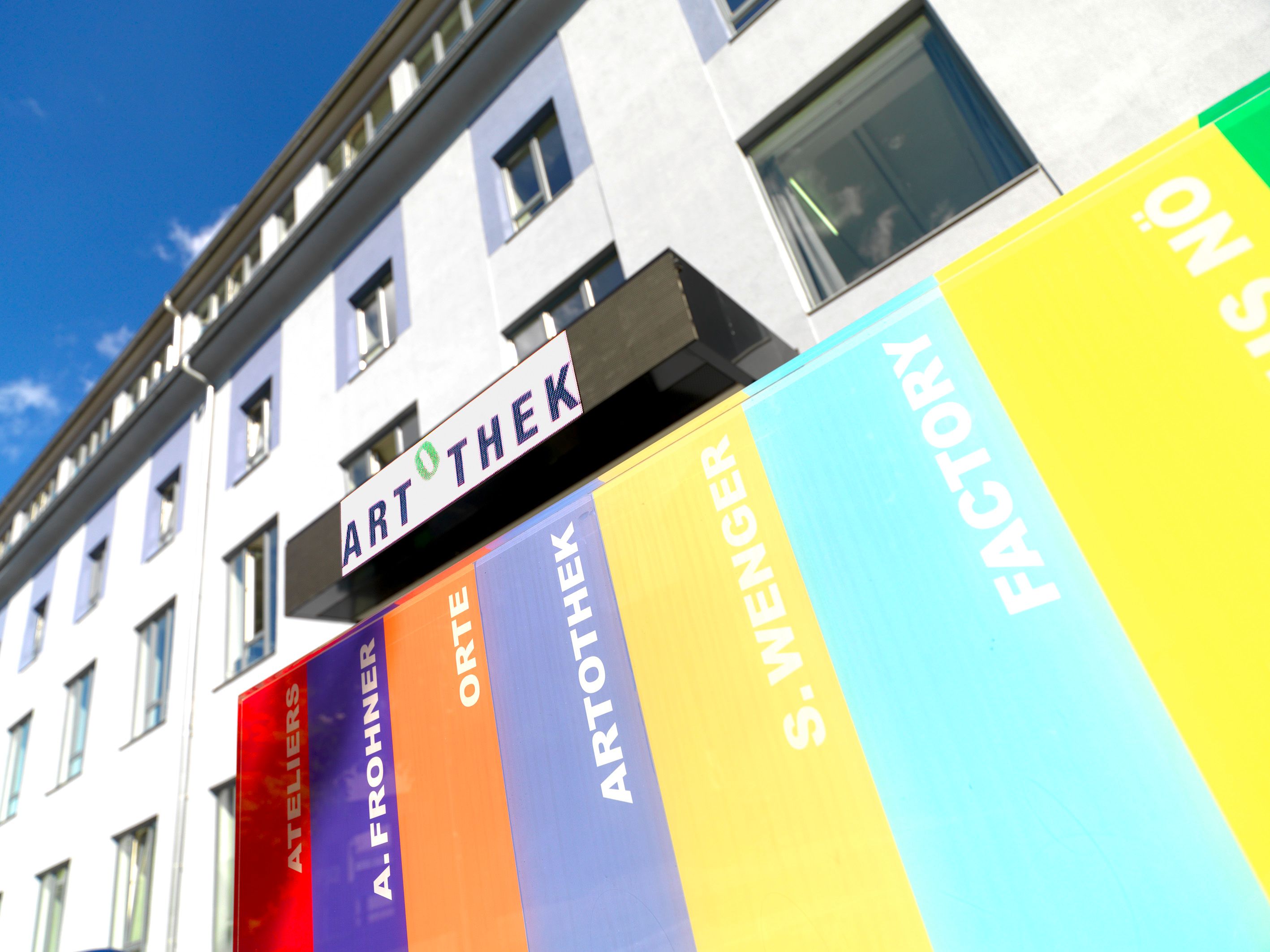 Exterior view of a building with Artothek sign and colorful stripes.