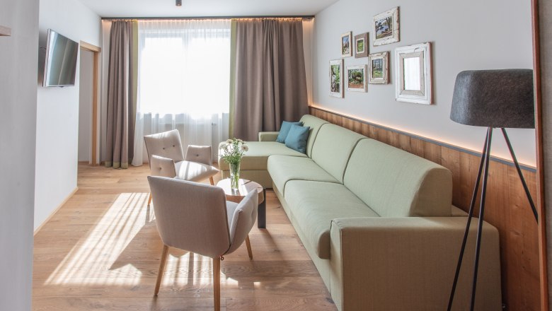 Bright hotel room with green couch, two armchairs, wooden floor and murals.