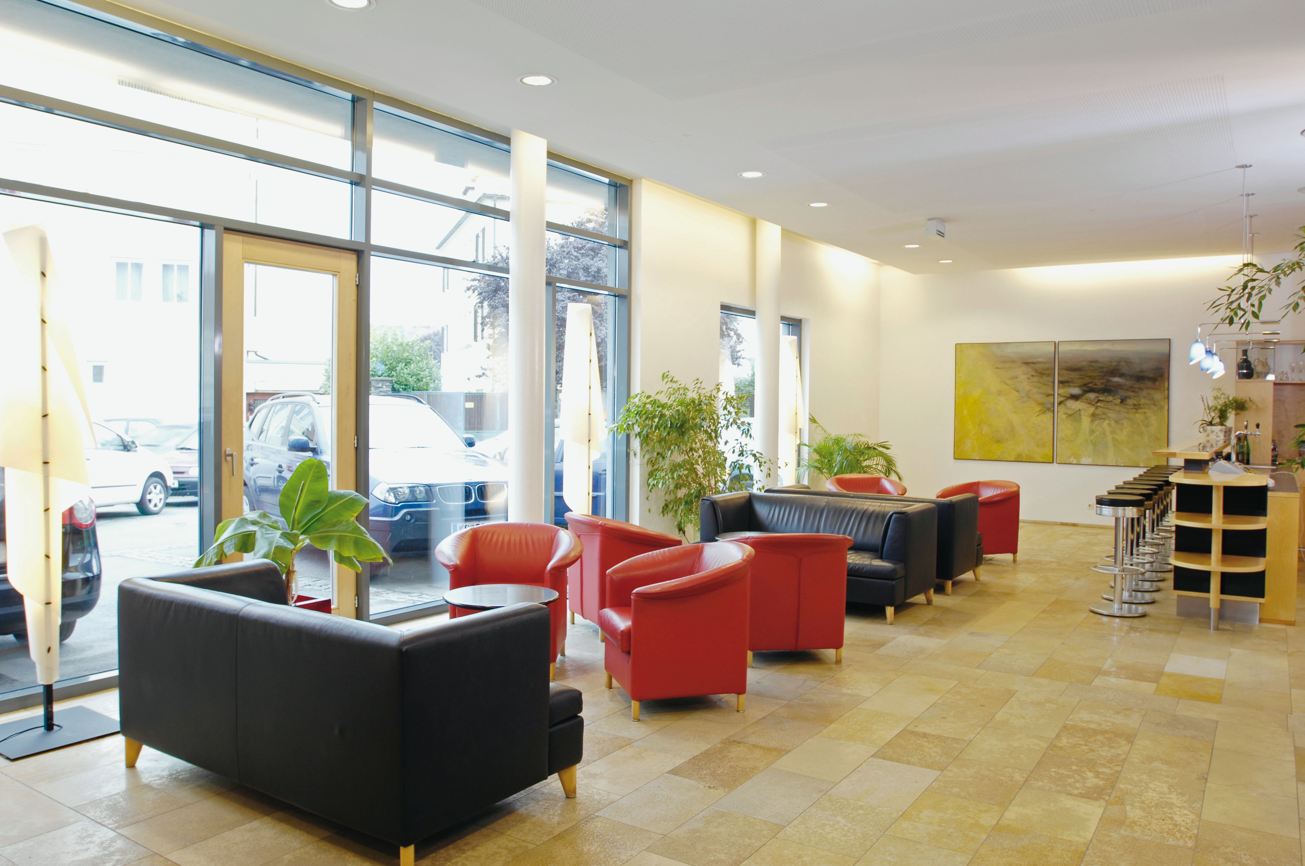 Bright hotel lobby with red and black armchairs, bar stools and large windows.