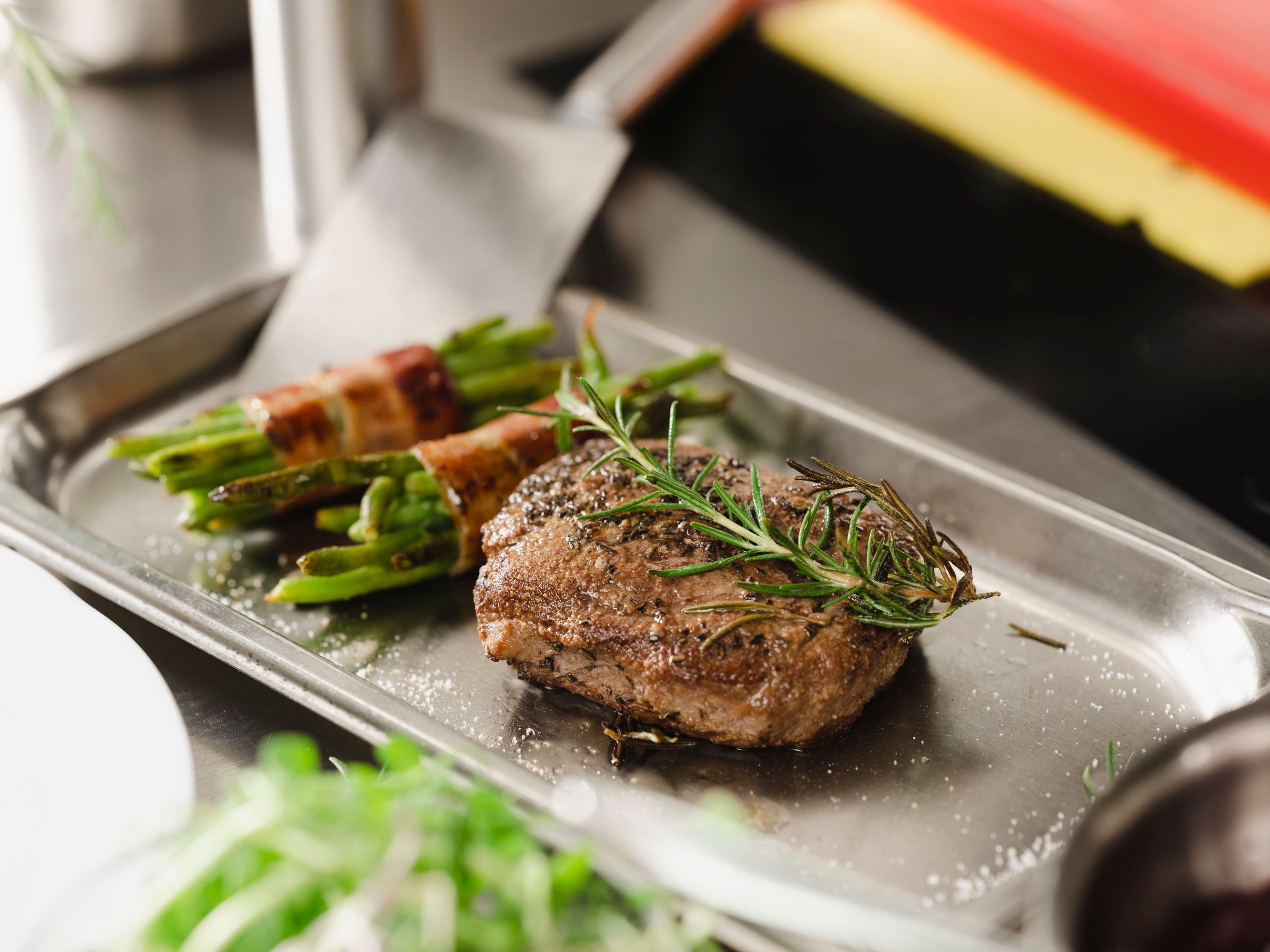A steak with rosemary and beans wrapped in bacon on a metal tray.