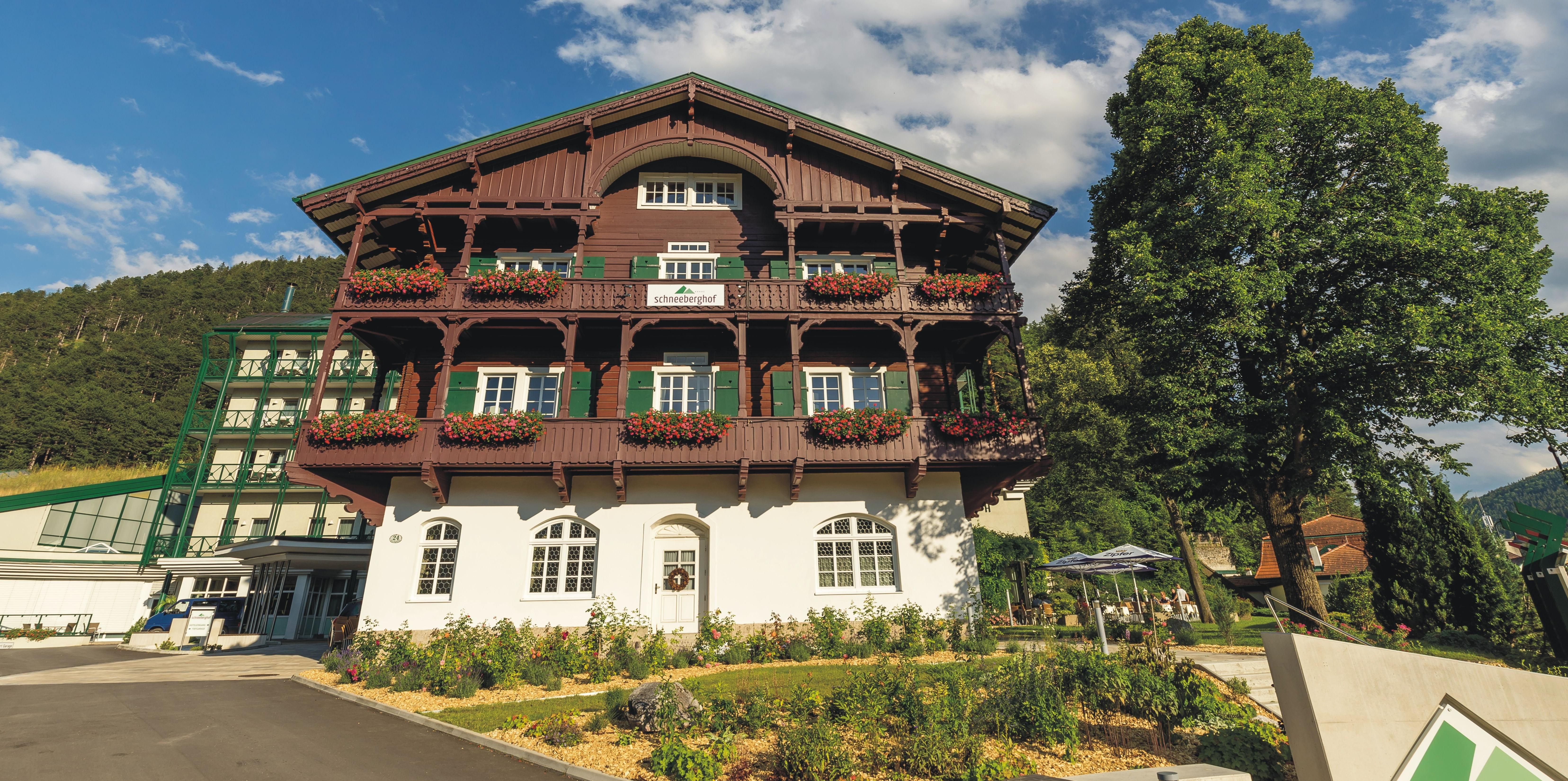 Hotel Schneeberghof with a balcony decorated with flowers and blue sky.