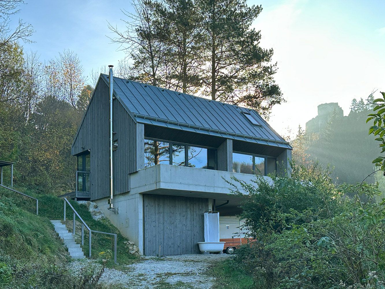 Modern house with wooden façade and large windows in wooded surroundings.