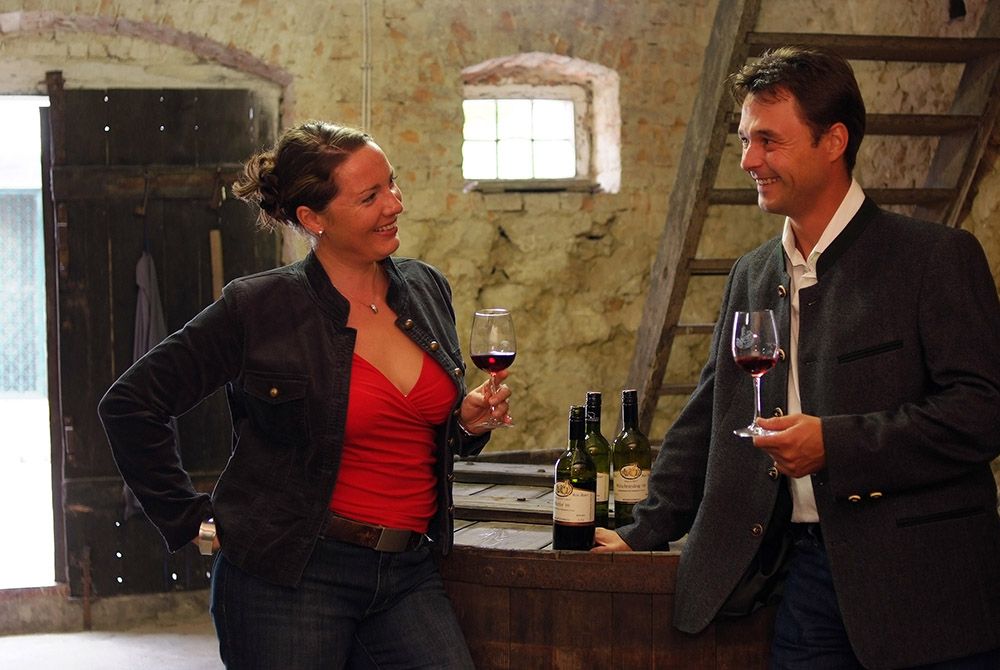Two people at a wine tasting in a rustic room.