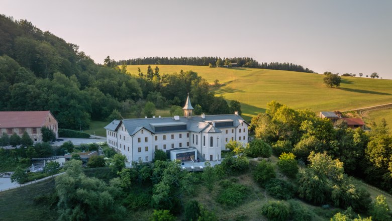 Refugium Hochstrass, © Niederösterreich Werbung / Maximilian Pawlikowsky Aerial view of a large white building in a green landscape.