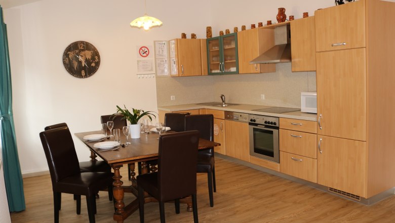 Dining area with wooden table and chairs, next to a modern kitchen with wooden cupboards.