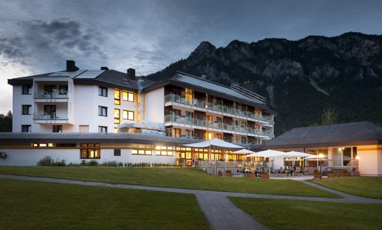 An illuminated hotel building against a mountain backdrop at dusk.